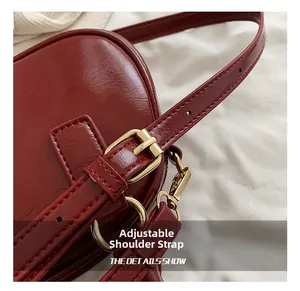 Close-up of adjustable shoulder strap with gold buckle on burgundy leather handbag
