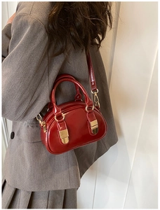 Detail of red patent leather bowling bag worn by model over a dark grey blazer