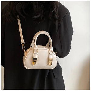 Detail of a creamy white bowling bag with gold buckles worn over a black blazer