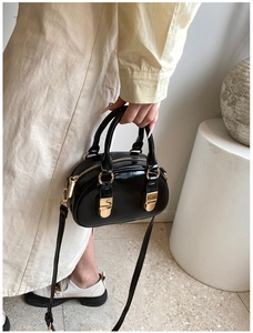 Detail of black glossy bowling bag with gold hardware held by a model in a white dress