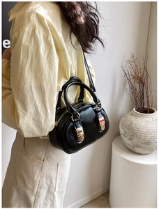 Detailed view of black glossy leather handbag with gold hardware on a minimalist background