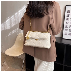 Detail of cream quilted crossbody bag with gold chain strap and metallic pendant charm