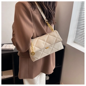 Detail of a quilted cream shoulder bag with gold chain strap and metal logo charm