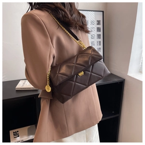 Close-up of brown quilted chain bag featuring a gold square lock and metallic pendant