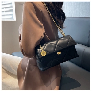 Detail of a black quilted leather crossbody bag with a chunky gold chain and metal charm