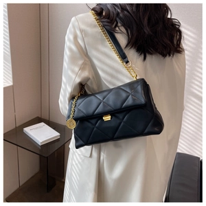 Detail of a black quilted chain bag with gold hardware worn on a white blazer