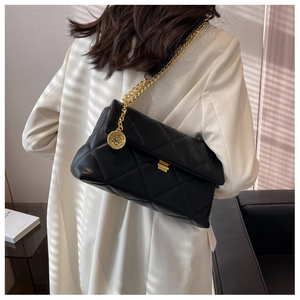 Detailed shot of black quilted bag with gold chain strap and metal pendant on a white suit