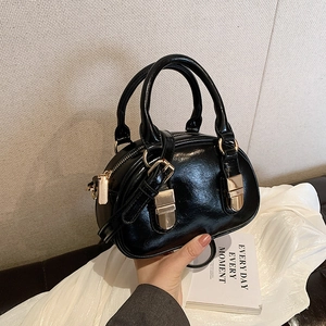Glossy black bowling bag with golden buckles and dual handles shown in a lifestyle setting