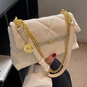 Quilted beige shoulder bag with gold chain strap and metal logo tag in a stylish setting