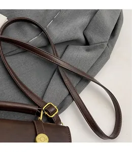 Detail of dark brown leather crossbody bag with vintage gold metal buckle and smooth strap