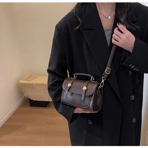 Detail view of a vintage dark brown leather crossbody bag styled with a black blazer