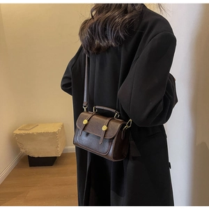 Detailed side view of vintage dark brown crossbody bag with gold buckles on black coat