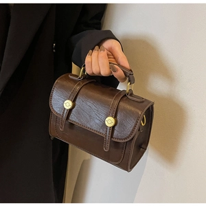 Close-up of vintage brown leather square bag featuring golden metal turn-lock and strap detail