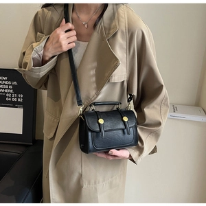 Detail of classic black PU leather shoulder bag with gold metal buckle on beige trench coat