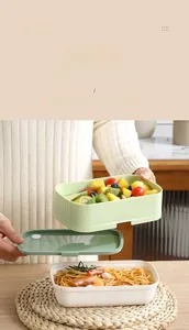 Detail of a green and white stackable lunchbox with separate layers for pasta and fruit