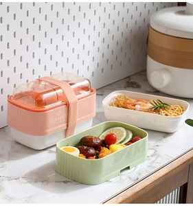 Three-layer bento box with elastic strap, filled with pasta and salad in a modern kitchen