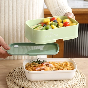 Stackable bento lunch box held by hands showing internal layers with fresh food and pasta