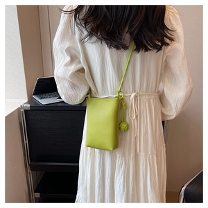 Detail of lime green mini crossbody bag with litchi texture and decorative woven charm