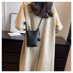 Detail of a minimalist black textured leather crossbody bag with decorative knotted ball