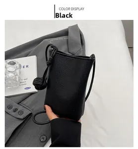 Detail of black lychee grain mini shoulder bag with leather knot on grey blazer
