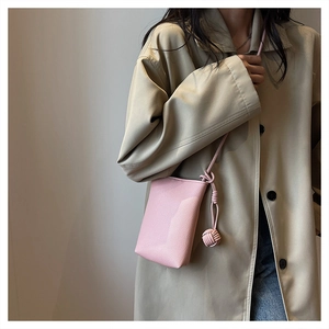 Detail of pink pebbled leather crossbody phone bag with minimalist knot strap on beige coat