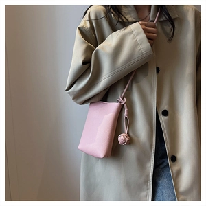 Pink lychee texture mini crossbody bag with knot charm worn with a beige trench coat
