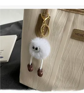 Detail of a white plush monster charm with googly eyes and gold clip on a leather bag