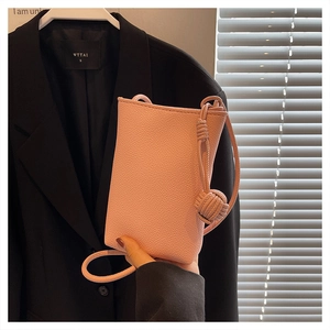Detail of light pink lychee grain leather crossbody bag with decorative knot strap