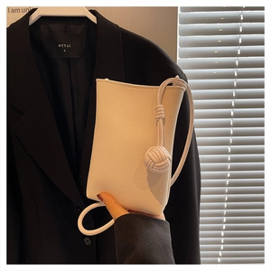 Close-up of white pebble grain leather mini crossbody bag with knotted rope strap detail
