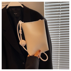 Detail of white leather mini crossbody bag with litchi texture and woven ball charm