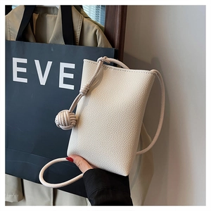 Close-up of cream-colored litchi grain leather mini crossbody bag with woven ball charm