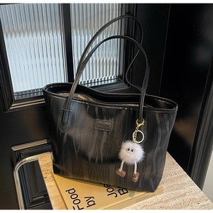 Detail of black tote bag with wave texture fabric and a white plush keychain
