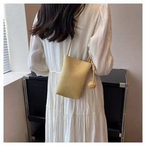 Detail of yellow lychee leather mini crossbody bag with a woven knot charm on white dress