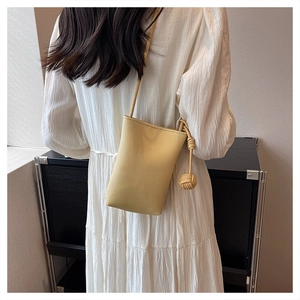 Mini pastel yellow crossbody bag with litchi grain texture and woven ball pendant charm
