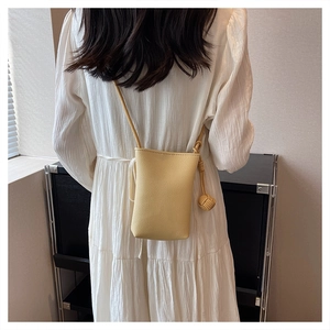 Detail of yellow mini leather crossbody bag with lychee texture and woven ball charm