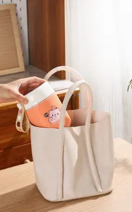 Tasse thermique orange avec motif d'ours placée dans un sac à main beige élégant