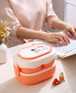 Detail of double-layer orange lunch box with side buckles and bear pattern on a desk