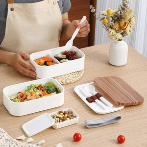 Minimalist double-layer white bento box with wood-texture lid and cutlery on a wooden table