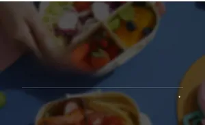 Macro shot of a bento box with compartments containing shrimp pasta and fruit salad