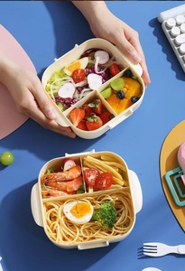Divided bento box with separate compartments showing salad, fruit, and pasta layout