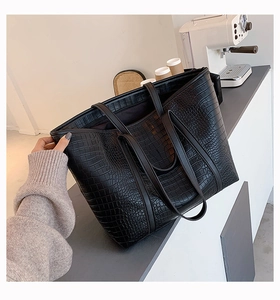 Detail of a large black tote bag with crocodile embossing on a cafe counter