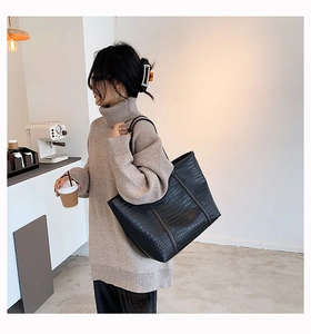 Detail of black crocodile texture tote bag worn by a model in a cozy cafe setting