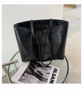 Detail of black crocodile-embossed tote bag with high-shine texture and sturdy shoulder straps