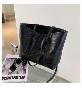 Close-up of black crocodile embossed texture on large capacity tote bag on glass table