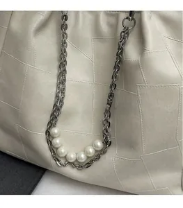Détail du sac seau en cuir crème avec coutures géométriques et chaîne de perles