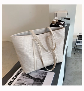 Detail of cream tote bag featuring textured crocodile pattern and dual shoulder straps