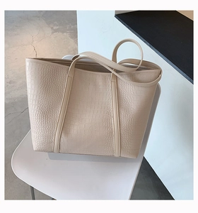 Close-up of beige tote bag featuring premium crocodile embossed texture on a chair