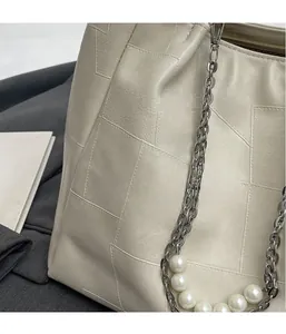 Détail du sac seau en cuir beige avec chaîne en métal argenté et bandoulière perlée