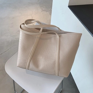 Detail of cream tote bag featuring textured crocodile pattern and long slim handles