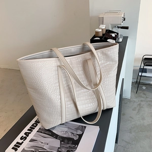 Detail view of a large cream tote bag featuring crocodile embossed leather texture on a table